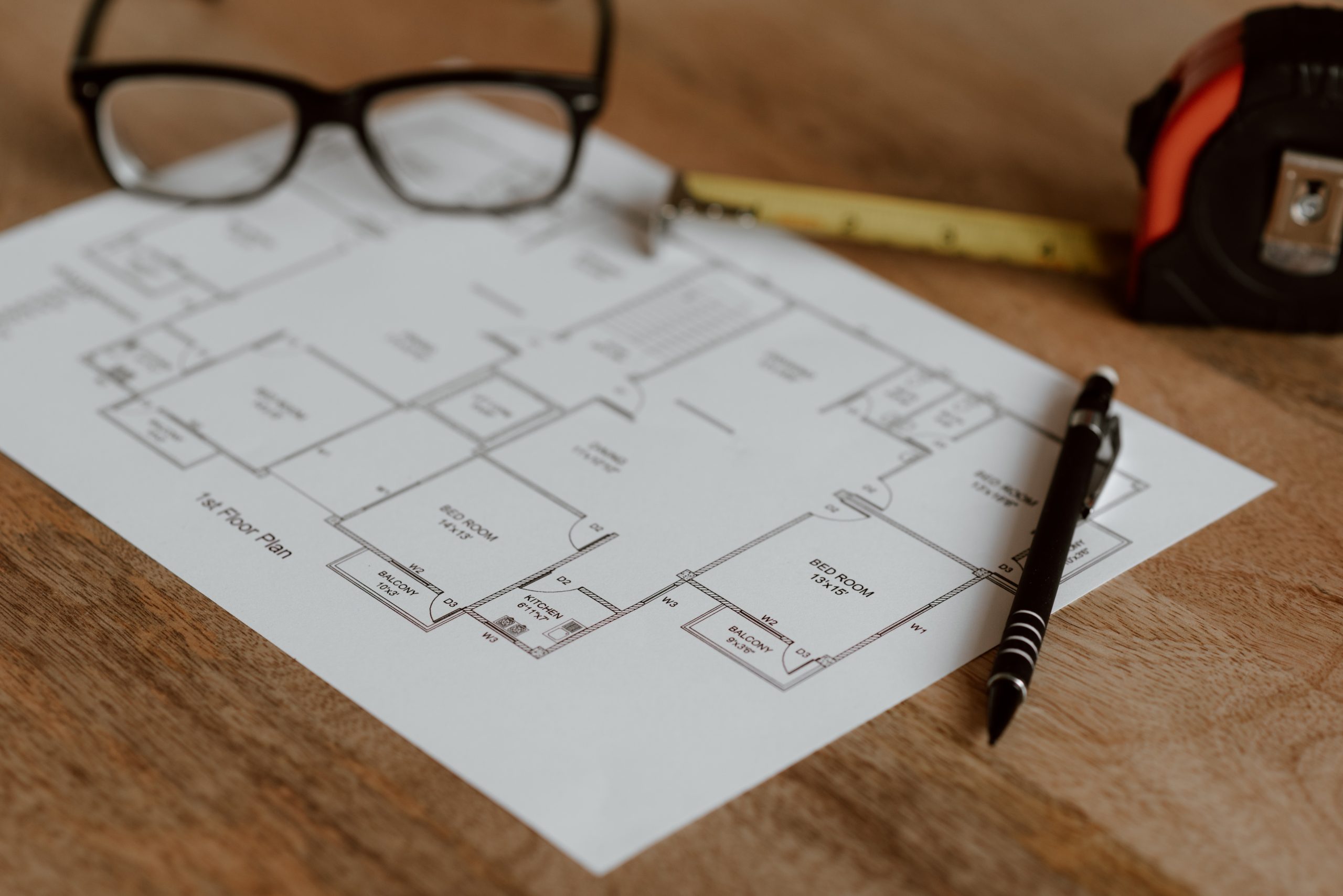 Floor plan on table with a pair of glasses, a pen and a tape measure.