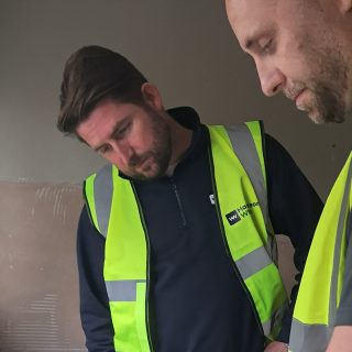 Two mean in hi-viz vests looking at housing plans