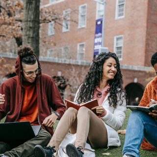 Three university students are sat on the grass outside a university building