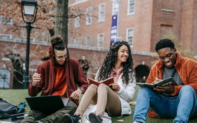 Three university students are sat on the grass outside a university building